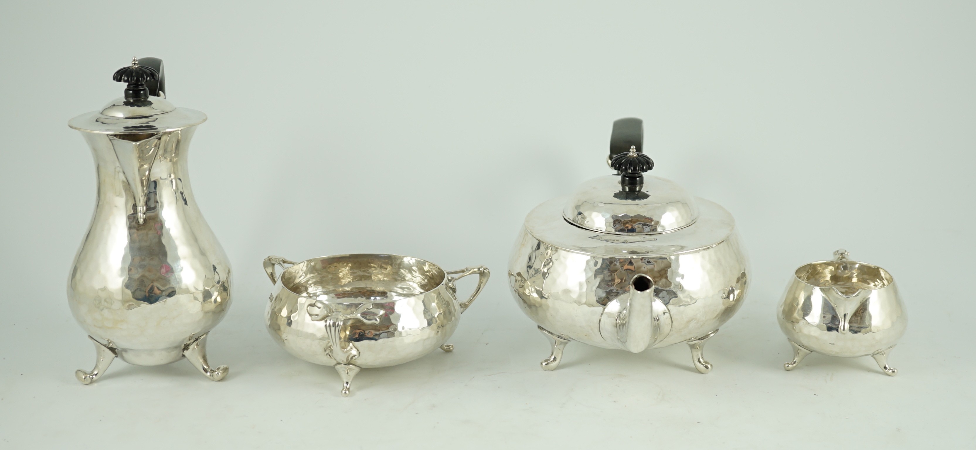 A George V Arts and Crafts three piece planished silver tea set and a similar hot water pot, by Charles Edwards